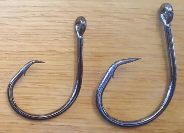 Two large circle hooks for catching catfish against a wooden board background