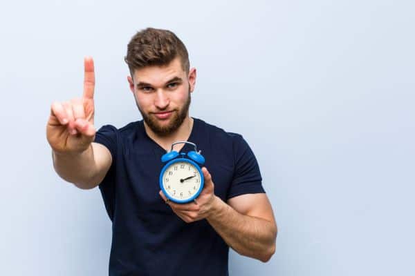 Man showing one finger with an alarm clock in his hand